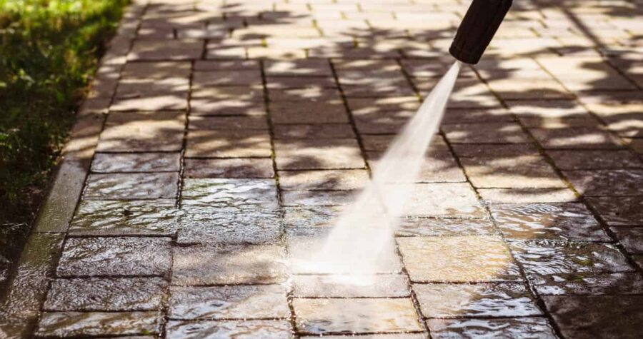 Person using a pressure washer to clean a hard surface, with high-pressure water spray visibly removing dirt