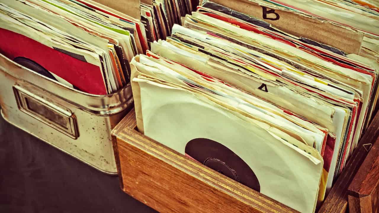 A stack of vinyl records piled unevenly, with colorful album covers partially visible, resting on a flat surface