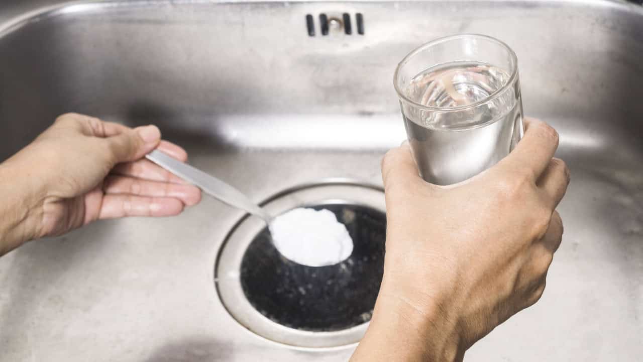 A hand pouring white powder into a dark bowl, glass of water nearby, kitchen setting