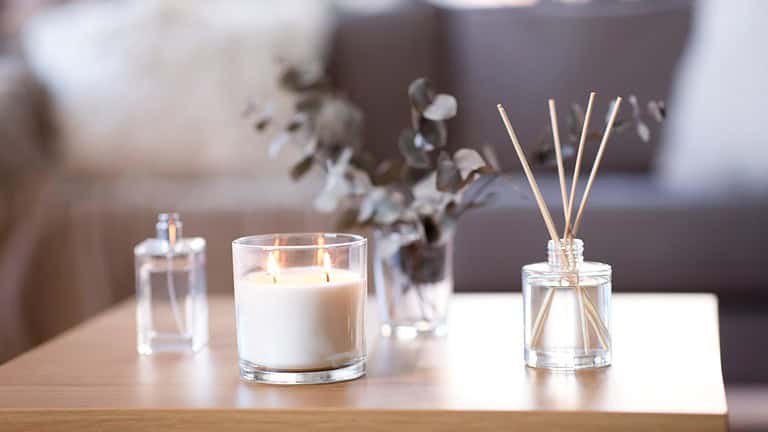 Candles and reed diffusers on a wooden table, lit candle in a glass container, glass vases with eucalyptus branches, home decor setup, relaxing ambiance