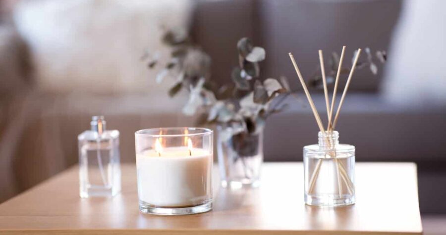 Candles and reed diffusers on a wooden table, lit candle in a glass container, glass vases with eucalyptus branches, home decor setup, relaxing ambiance