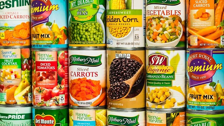 Cans of assorted vegetables, including mixed carrots, black beans, green peas, golden corn, garbanzo beans, and mixed vegetables, neatly arranged on a store shelf