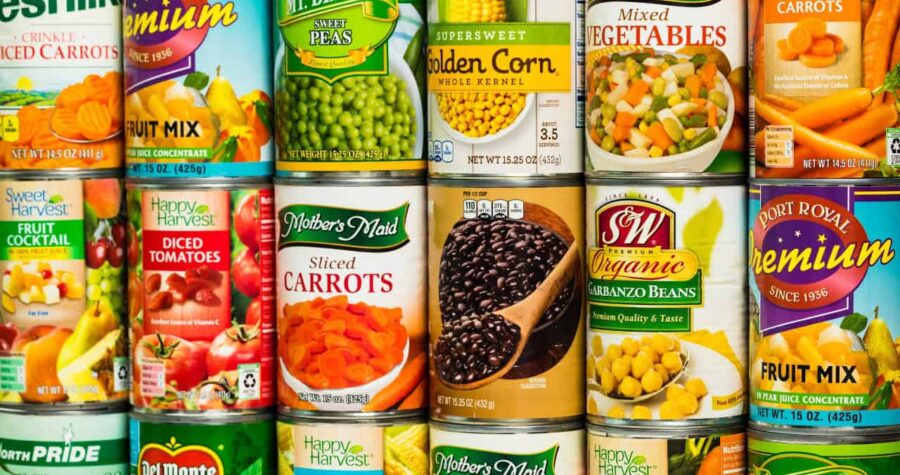 Cans of assorted vegetables, including mixed carrots, black beans, green peas, golden corn, garbanzo beans, and mixed vegetables, neatly arranged on a store shelf