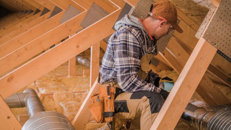 The worker is seated in an attic, installing insulation between wooden beams, conducting attic repairs or improvements, enhance energy efficiency in the home