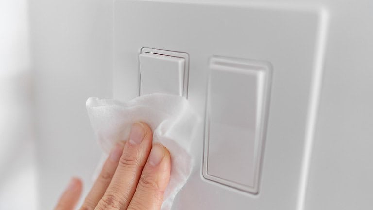 Person cleaning a light switch, wiping dust off, maintaining cleanliness, using a cloth, household cleaning task, cleaning home switchboard,