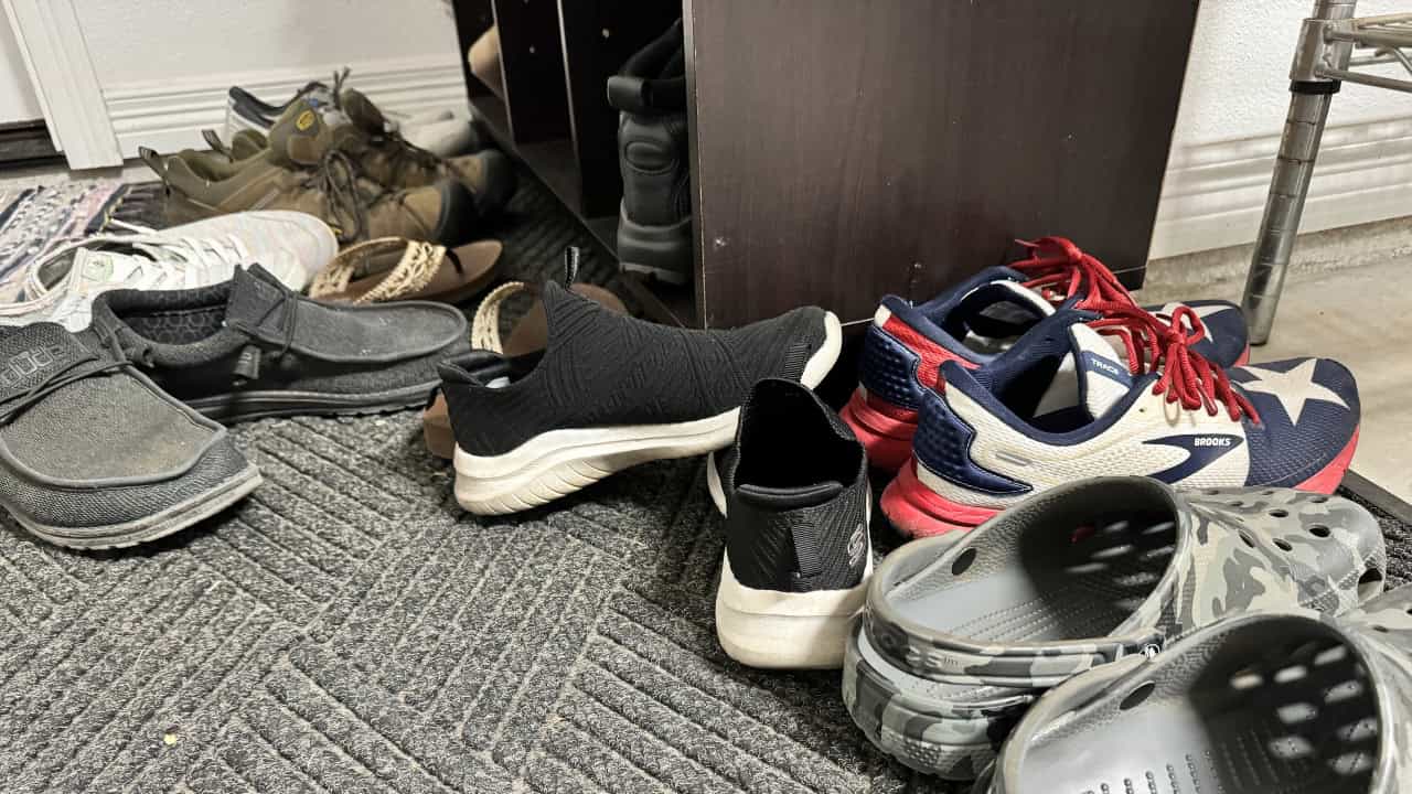 A collection of various shoes including sneakers and dress shoes arranged on a textured floor or mat near what appears to be an entryway or mudroom area