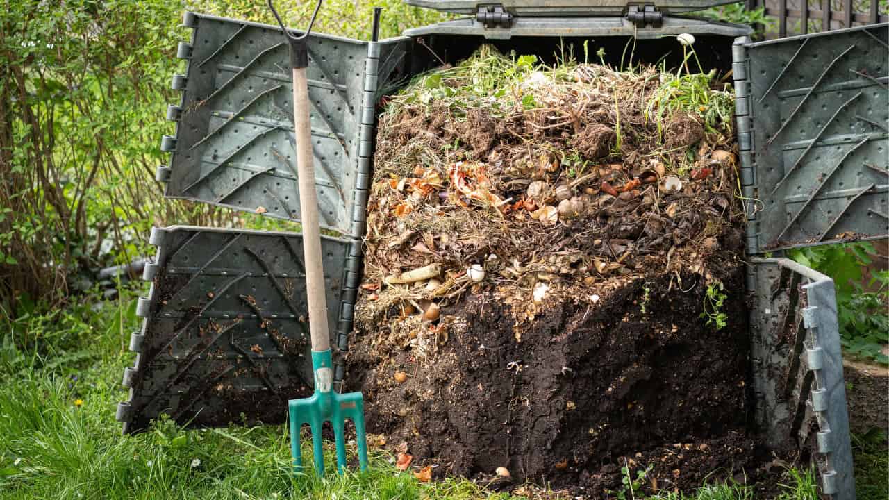 Large compost pile made of organic waste, including leaves, plant scraps, and soil, outdoors in a garden or farm setting
