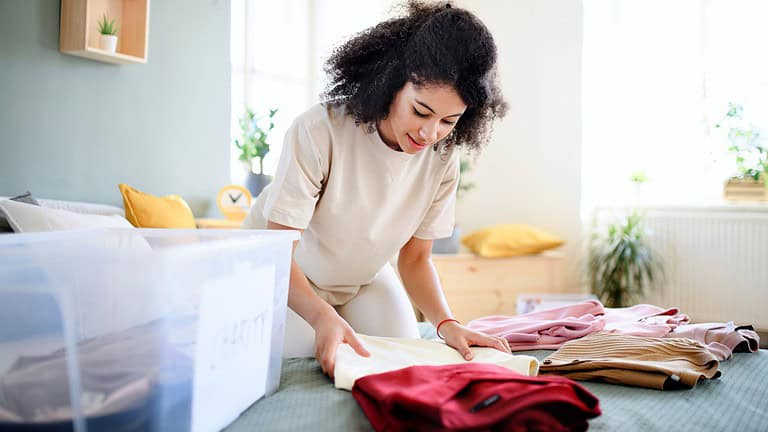 Woman folding clothes, sorting laundry, organizing items on a table, casual indoor setting, preparing for storage, maintaining neatness