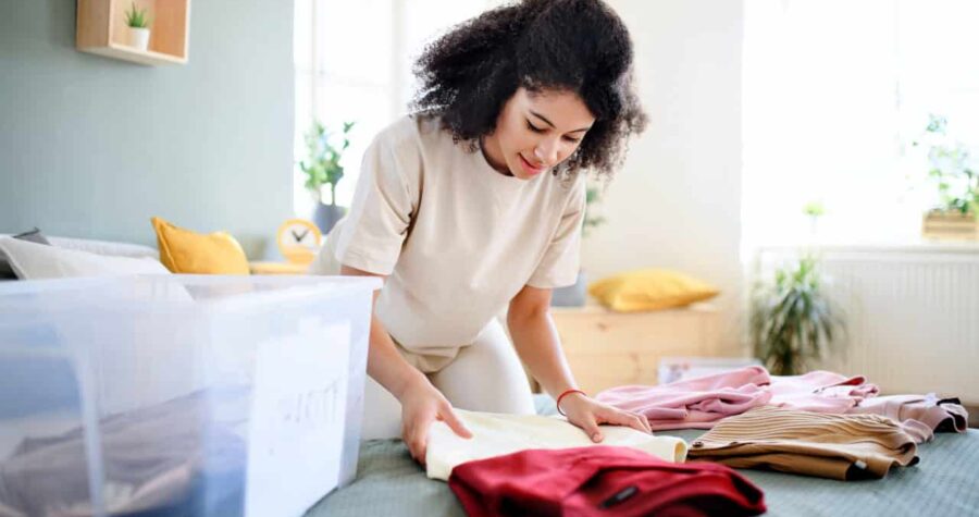 Woman folding clothes, sorting laundry, organizing items on a table, casual indoor setting, preparing for storage, maintaining neatness