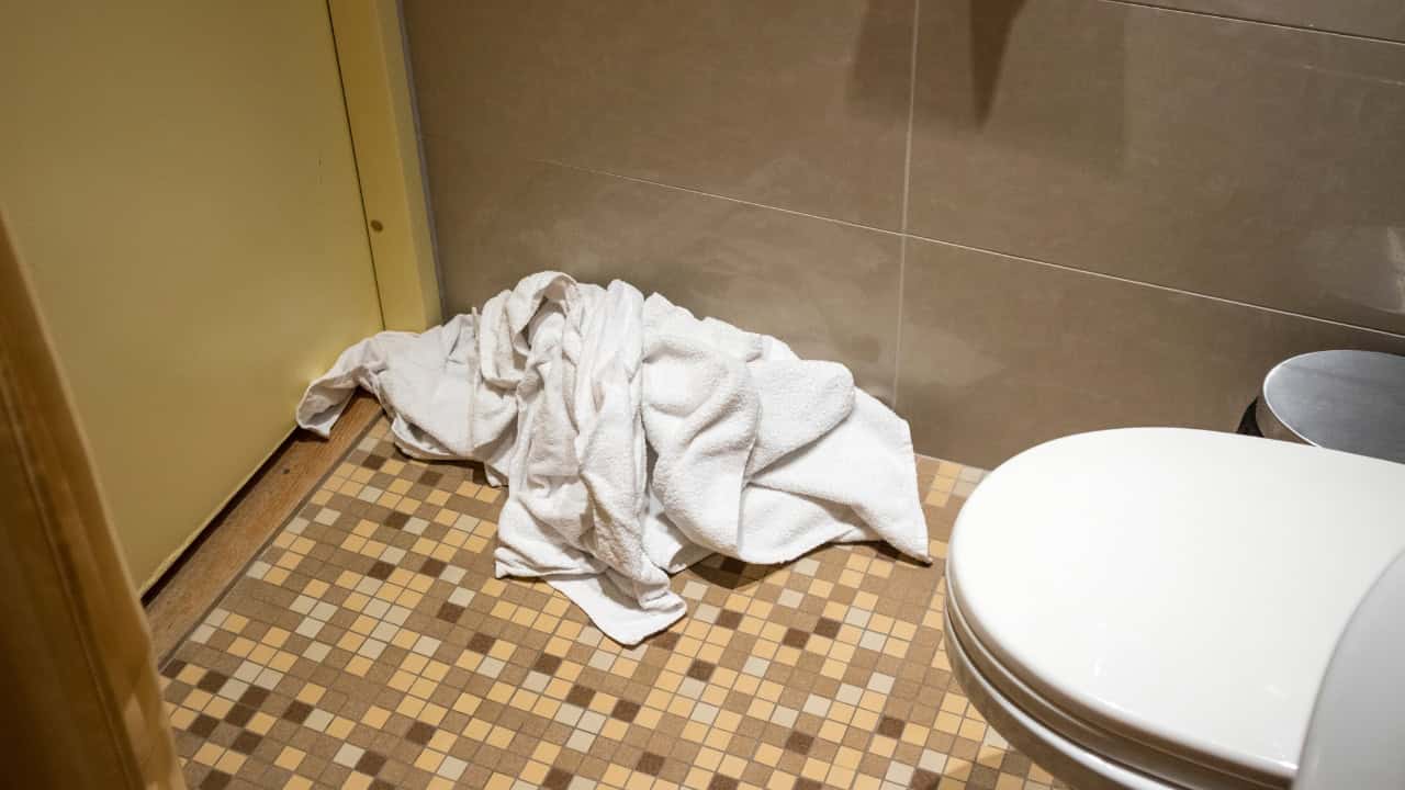 A crumpled white towel on the bathroom floor near a toilet, disorganized laundry, towel left on the floor, messy bathroom corner, towel carelessly placed, bathroom floor clutter, towel discarded after use