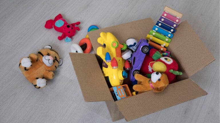 A cardboard box filled with children's toys, plush toys and colorful toy cars, a wooden xylophone and soft animal figures, scattered toys