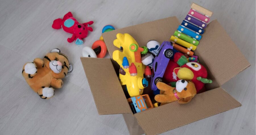 A cardboard box filled with children's toys, plush toys and colorful toy cars, a wooden xylophone and soft animal figures, scattered toys