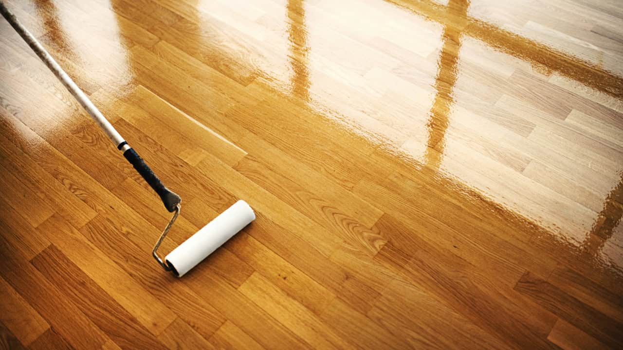 A roller applying a glossy finish on a wooden floor, enhancing durability and shine, reflecting natural light