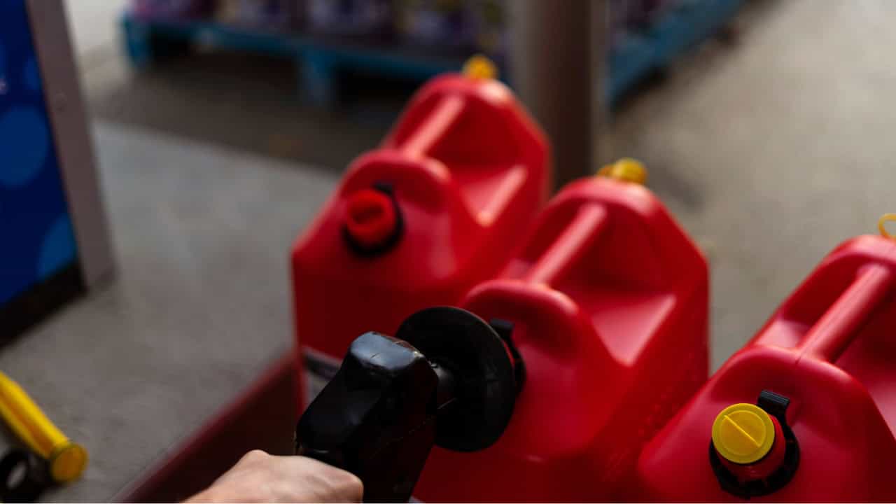 Red fuel cans being refilled, close-up of a person refueling gas containers, black fuel nozzle inserted into a red plastic gas can, emergency fuel storage, fuel supply preparation, refueling for generators or vehicles