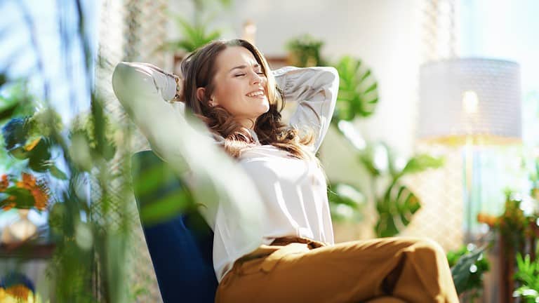 A person sitting in a relaxed position, with their arms behind their head, enjoying a moment of calm, surrounded by indoor plants