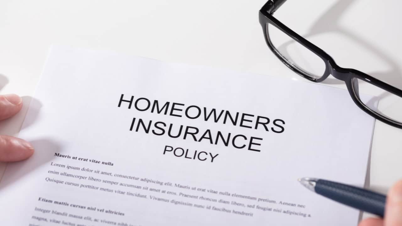 Homeowners insurance policy document with black pen, white paper background, blue checkmark icon visible