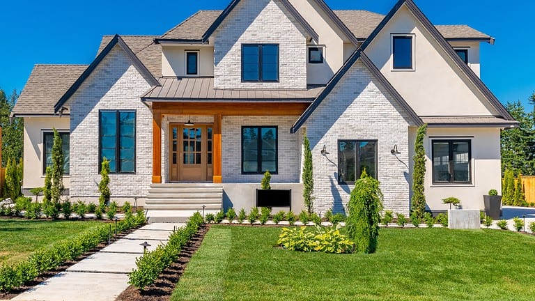 Modern farmhouse-style home with white brick exterior, black windows, wood accents, landscaped front yard, stone steps leading to entrance, neat lawn with young plantings
