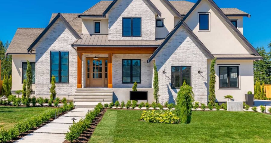Modern farmhouse-style home with white brick exterior, black windows, wood accents, landscaped front yard, stone steps leading to entrance, neat lawn with young plantings