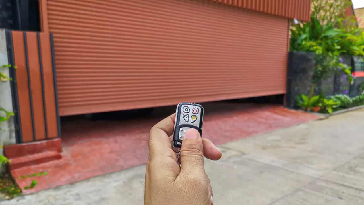 A hand holding a garage remote control, pointing at a closed garage door, the door's surface is textured, showing the action of opening or closing the garage, the remote control has several buttons, indicating use for an automated system