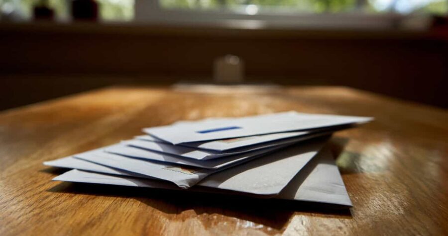 Stack of envelopes, placed on a wooden surface, soft natural lighting, mail on table, close-up view of envelopes, home office setting, letters awaiting attention