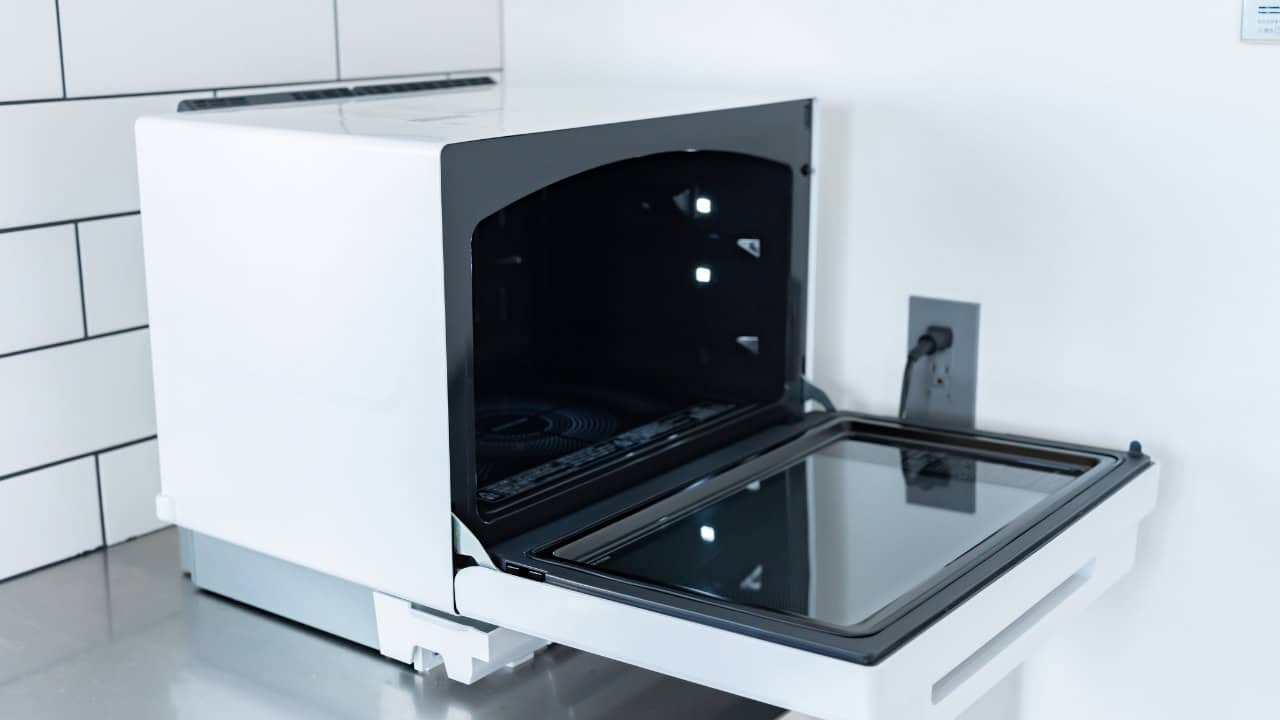 Open oven or microwave door showing dark interior with glass surface, metallic frame, appears to be part of kitchen appliance or laboratory equipment, partially visible control panel