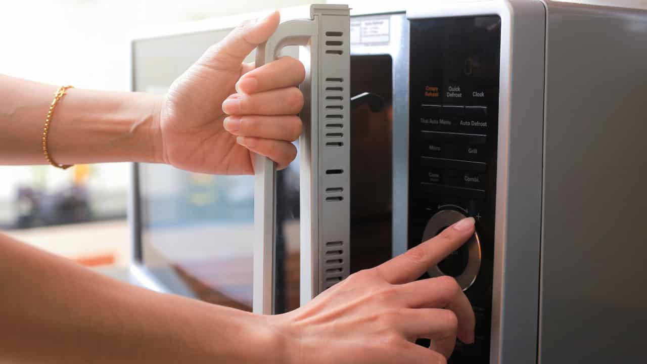 A person adjusting the timer on a microwave while holding the door handle, preparing to use the appliance