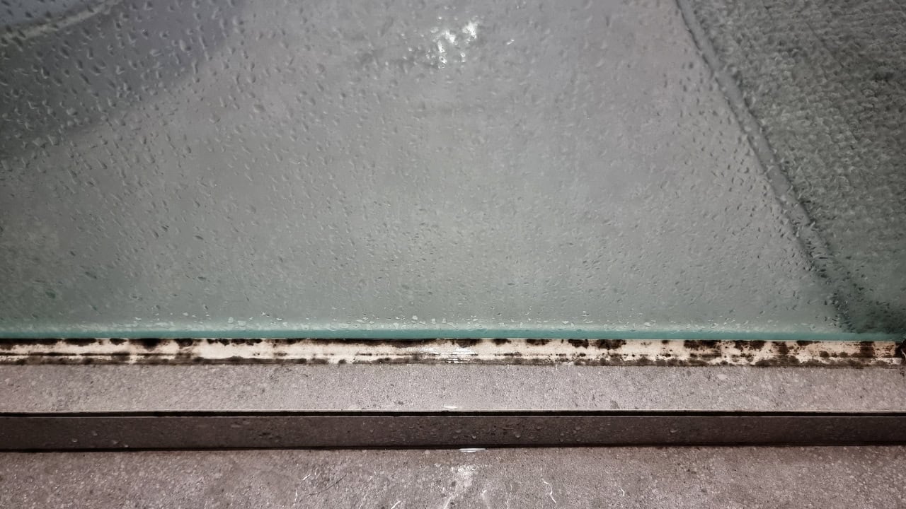 Bathroom caulking line, white silicone sealant between tub and wall, slight mold or discoloration visible along seam, gray wall surface