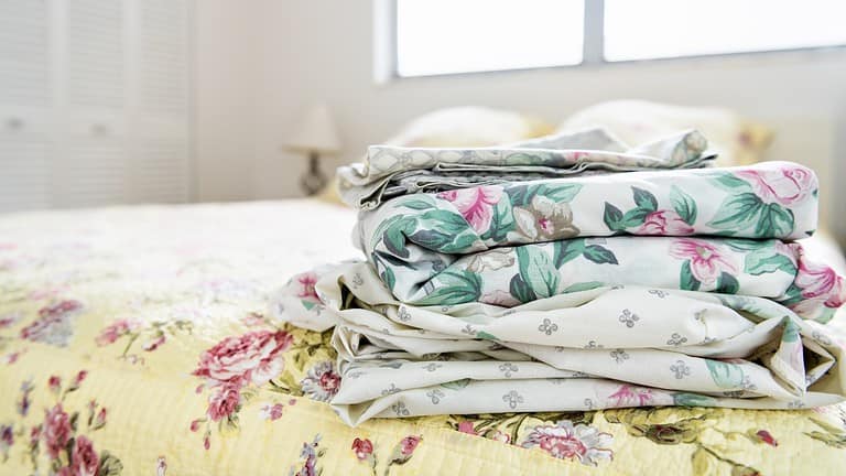 Stack of neatly folded floral bedsheets, placed on a bed, bedroom setting with soft lighting, fresh linens prepared for use, cozy and inviting atmosphere