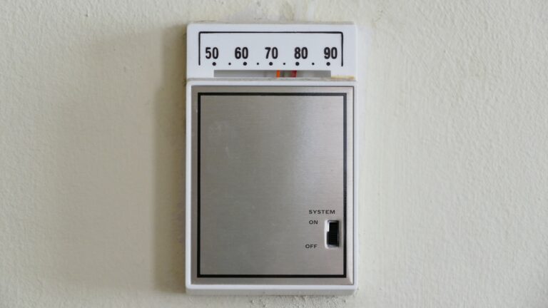 Digital thermostat on wall, set between 60 and 70 degrees, simple design, temperature control for indoor comfort, wall-mounted unit, adjustable temperature settings, basic temperature control device