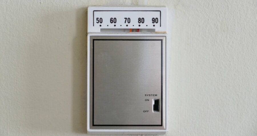 Digital thermostat on wall, set between 60 and 70 degrees, simple design, temperature control for indoor comfort, wall-mounted unit, adjustable temperature settings, basic temperature control device