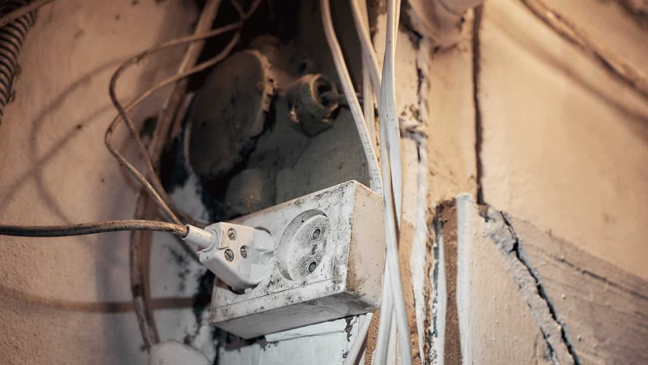 Damaged interior wall showing exposed wiring, insulation, and wooden studs, construction or renovation in progress
