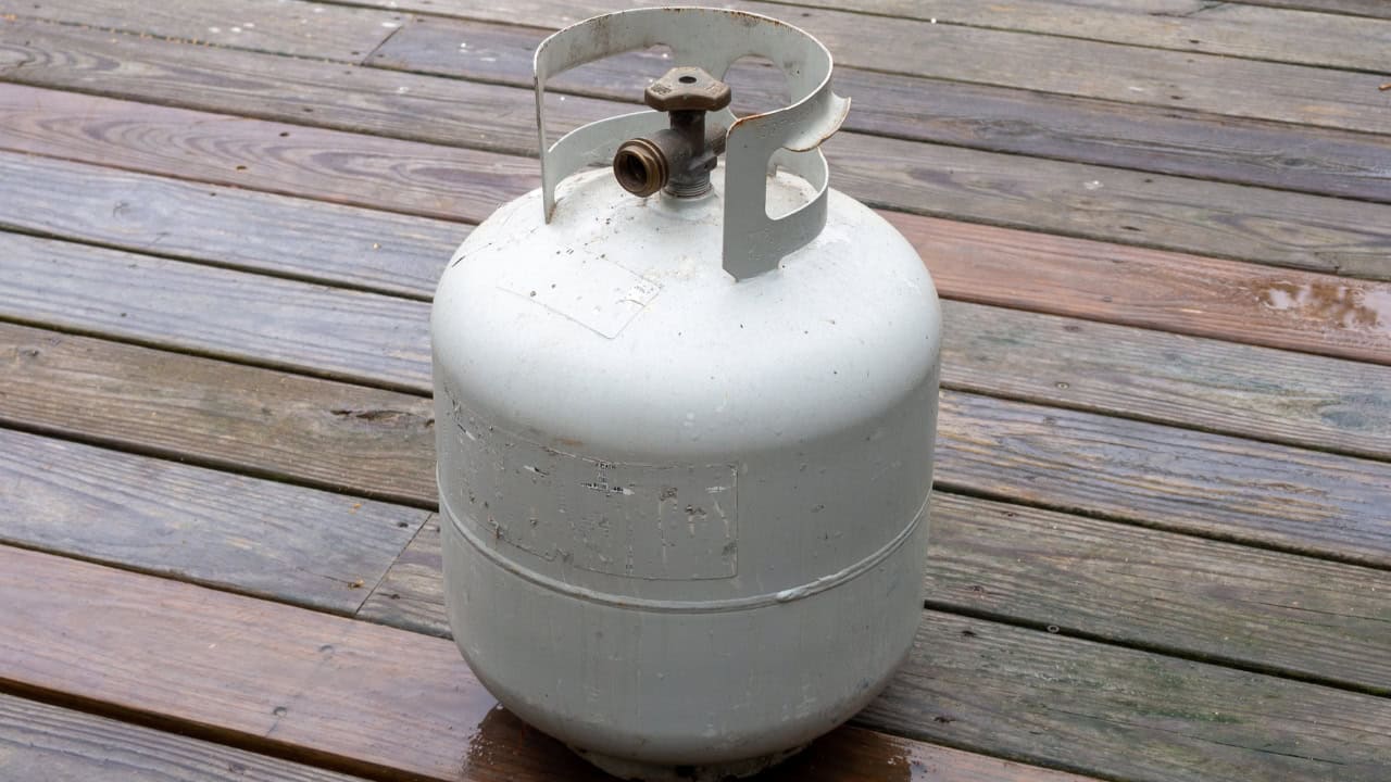 White propane gas tank, placed on a wooden deck, metal valve on top for gas flow control, portable and refillable fuel source