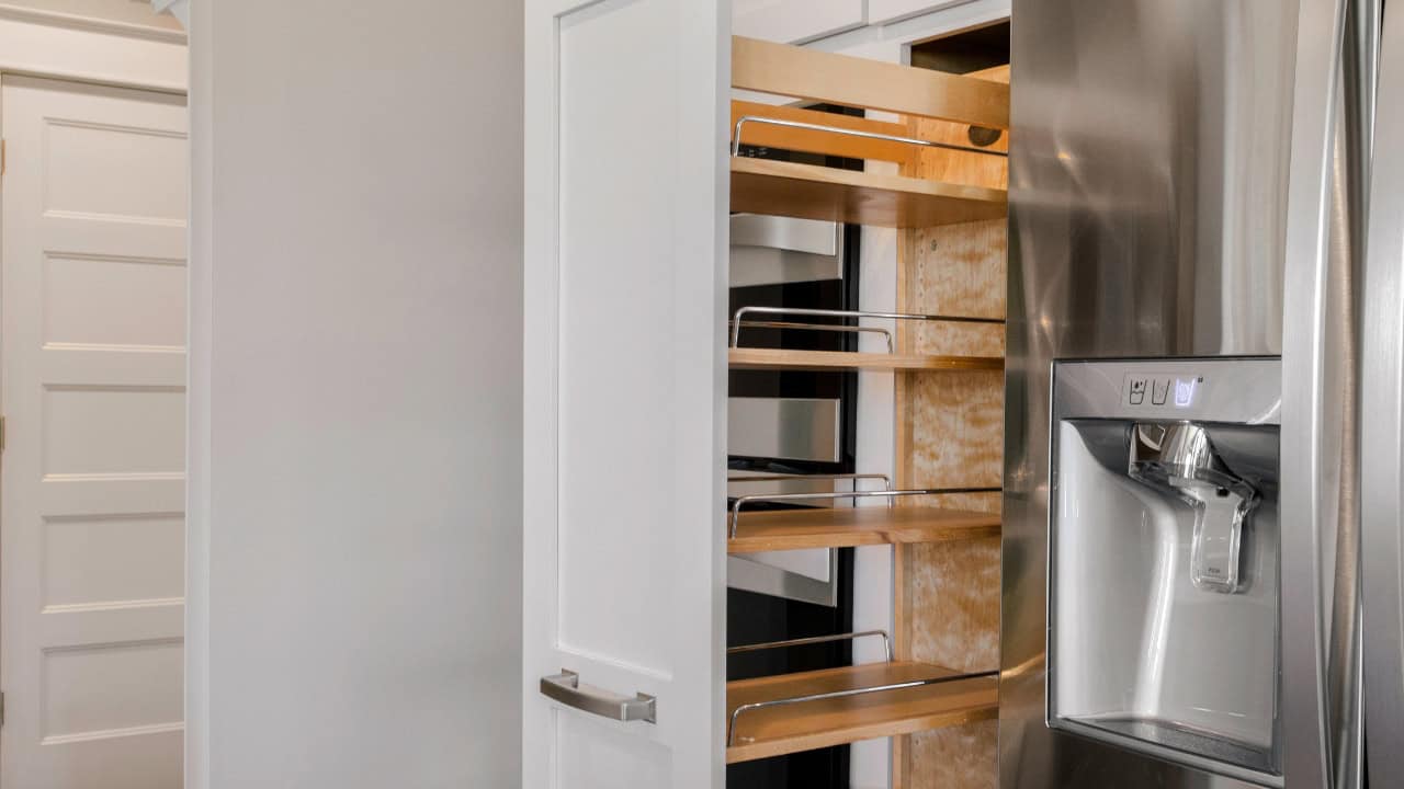 A modern pull-out pantry with wooden shelves and metal rails, partially extended beside a stainless steel refrigerator