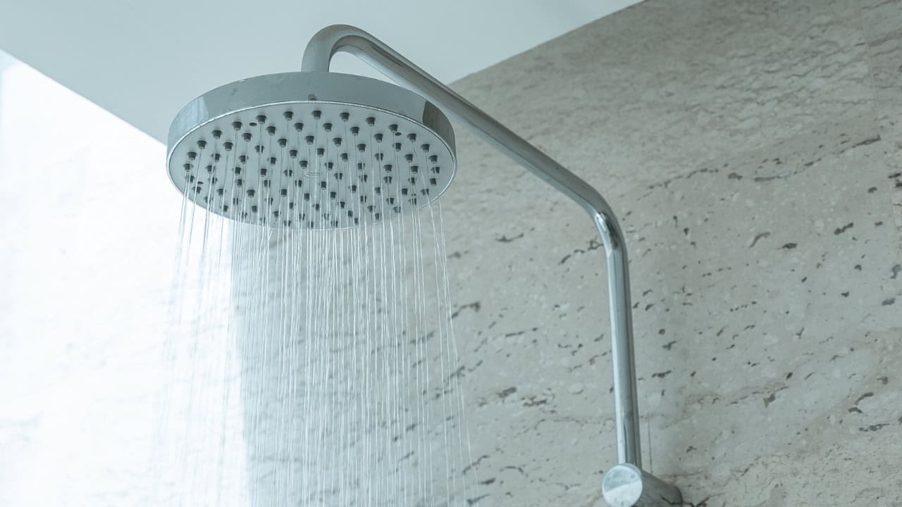 Modern rainfall shower head mounted on white tiled wall, water streaming down from multiple nozzles, bathroom shower in use, minimalist design