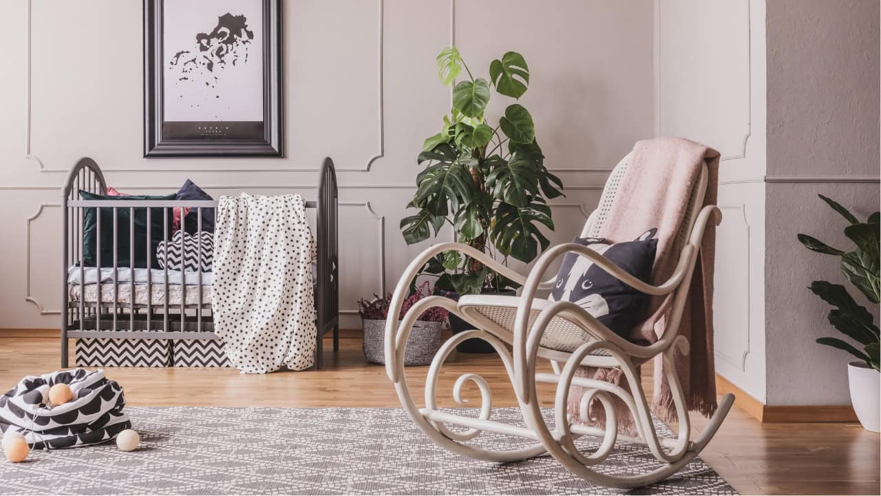 Cozy living space, wooden rocking chair, soft blanket draped over chair, houseplant in corner, crib with patterned blanket, framed artwork on wall, elegant interior design, warm and inviting atmosphere