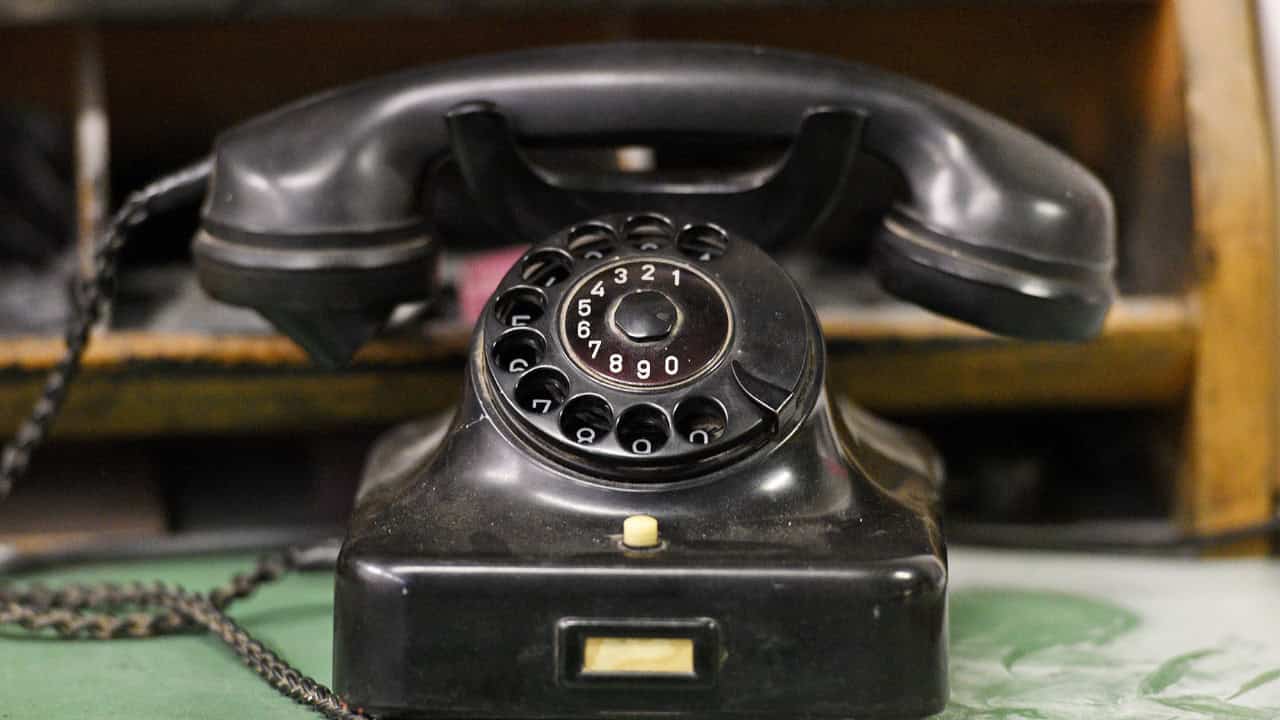 A close-up of a vintage black rotary phone, featuring a circular dial with numbers 0-9, a small button below the dial, and a receiver attached, evoking a nostalgic, classic telephone design