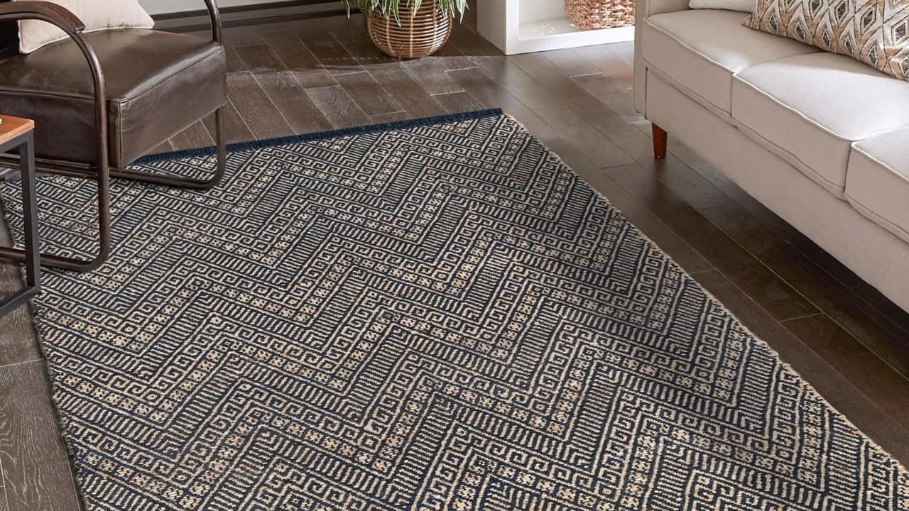 A decorative patterned rug on a wooden floor, herringbone design, beige and navy color scheme, placed in a living room area, adding comfort and style, complementing the furniture