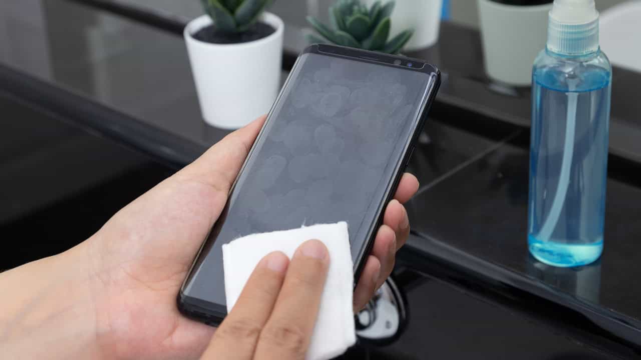 Hand cleaning a smartphone screen with a cloth, removing fingerprints and smudges, ensuring a clear display, maintaining device hygiene