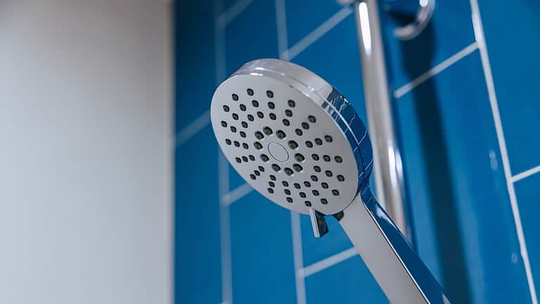 White handheld shower head mounted on blue tiled bathroom wall, multiple spray nozzles visible, adjustable shower fixture in clean bathroom setting