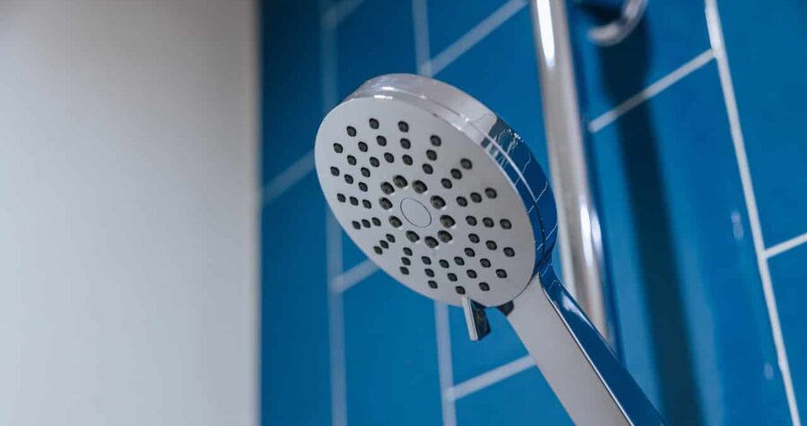 White handheld shower head mounted on blue tiled bathroom wall, multiple spray nozzles visible, adjustable shower fixture in clean bathroom setting