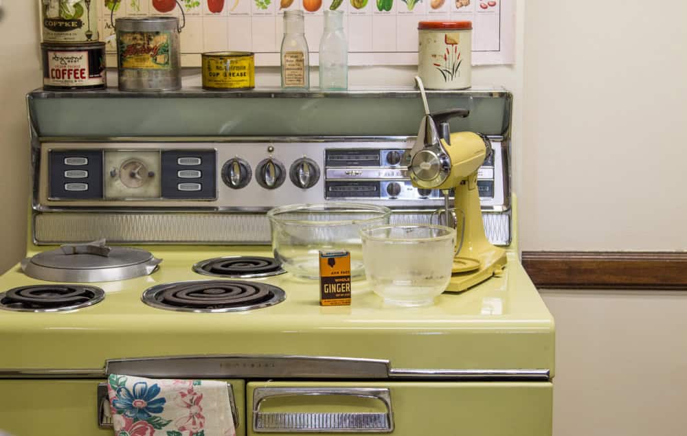 Vintage yellow stove with round burners and retro dials, topped with mixing bowls, a yellow stand mixer