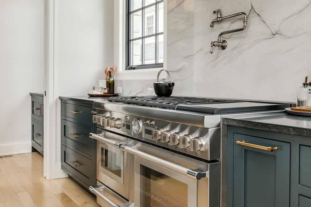 Modern stainless steel gas range, double oven with multiple burners, marble backsplash with pot filler faucet, bright kitchen with natural light, high-end cooking appliances, elegant and functional kitchen design