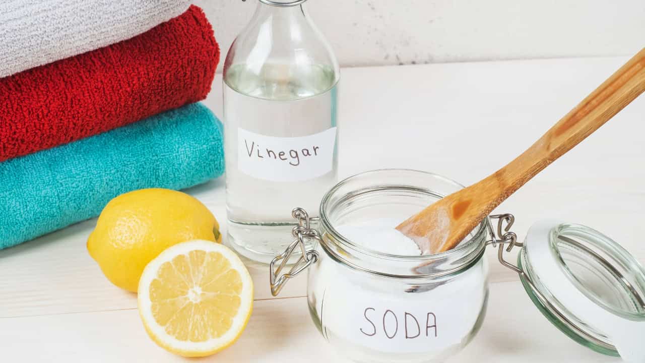 a bottle labeled "Vinegar," a jar labeled "Soda," a lemon half, colorful washcloths