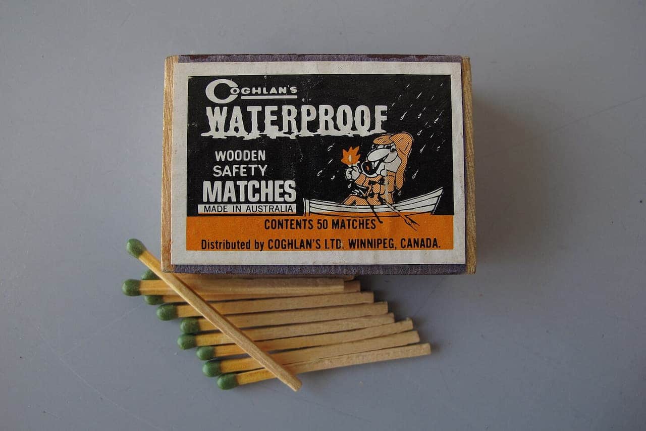 Coghlan's waterproof wooden safety matches box with cartoon character in rain, with eight green-tipped matches displayed below