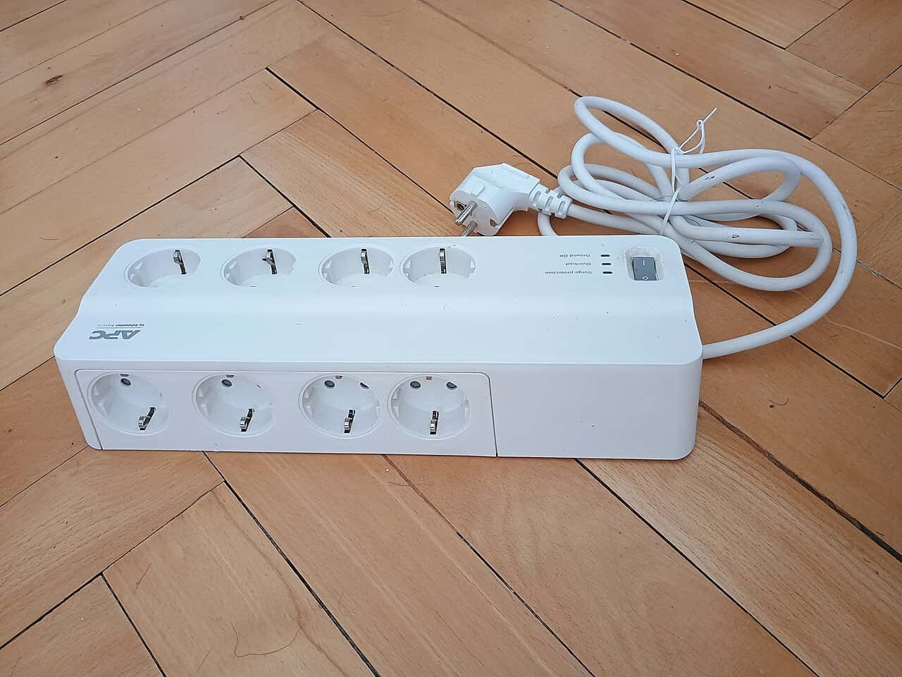 White power strip with six outlets, long cord attached, power switch to control the flow of electricity, clean wooden floor background, ideal for connecting multiple devices