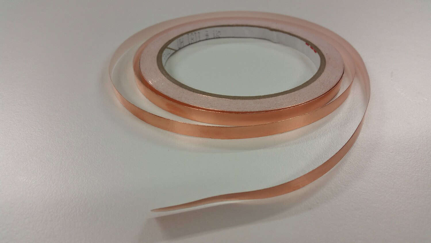 Roll of 5mm copper tape, coiled with a slight curl at the end, sitting on a white surface