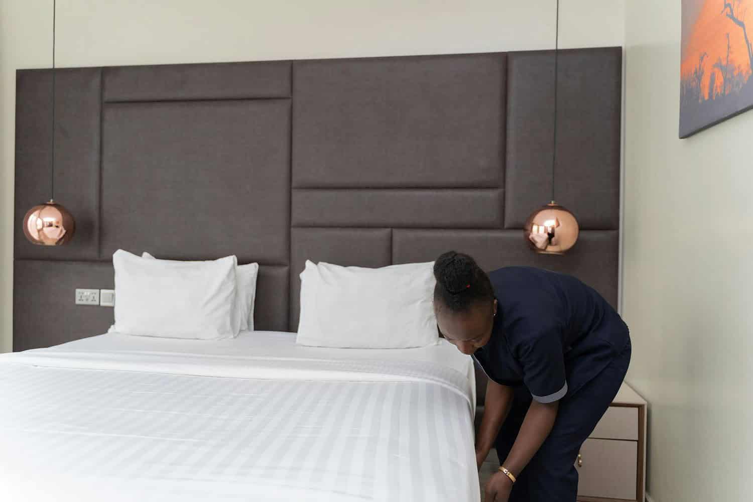 A hotel staff member prepares a bed in a sleek, modern hotel room with copper accents.
