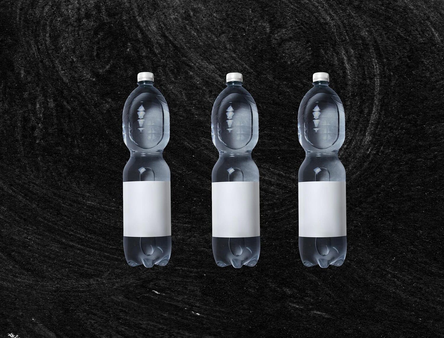 A set of three clear plastic water bottles on a textured black background, offering ample copy space