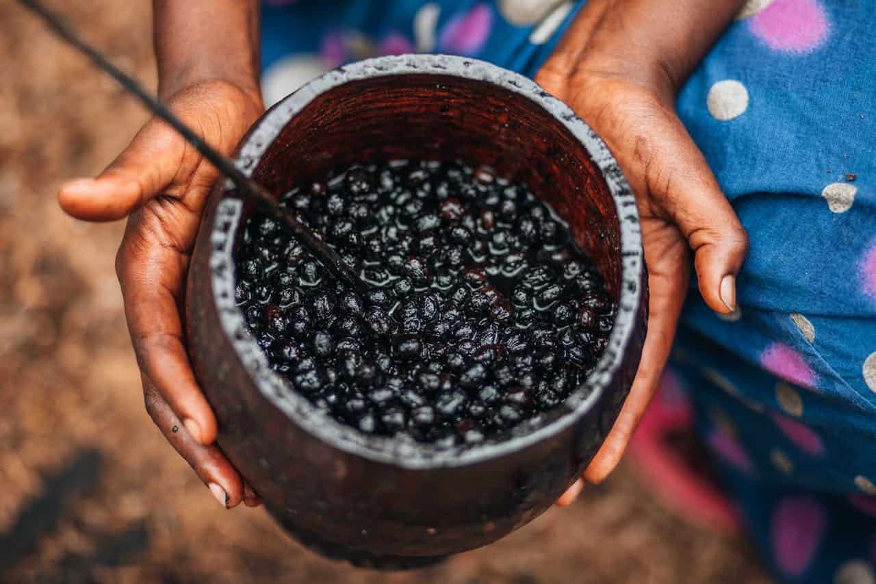Hands holding a rustic bowl filled with soaked acai berries, a metal spoon inside