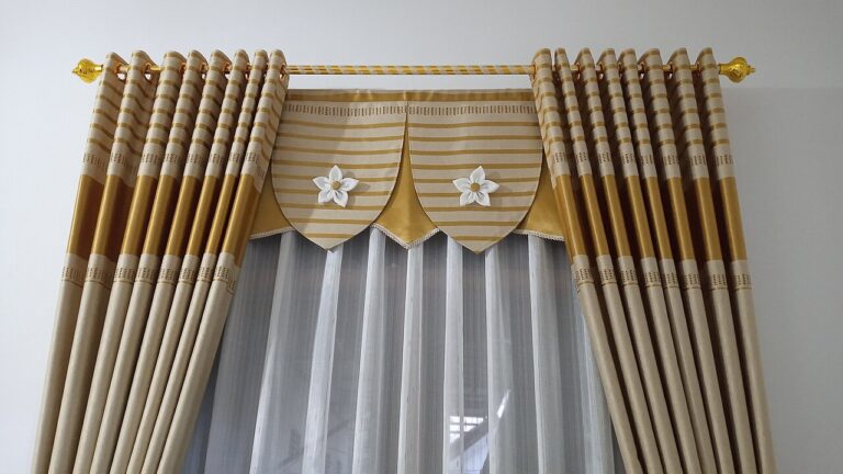 Elegant gold and beige striped curtains with decorative valance, white flower appliqués, sheer underlayer, gold finials on curtain rod, formal drapery treatment for living area